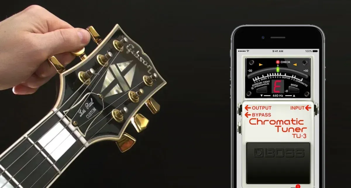 Mano girando una clavija del clavijero de una guitarra eléctrica junto a un celular con una app de afinador cromático