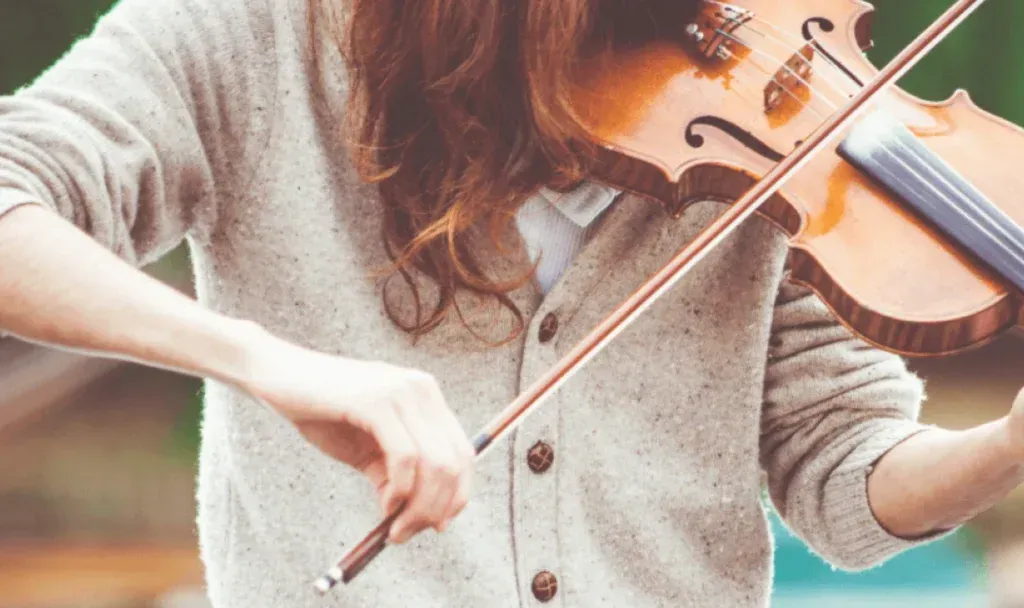 Persona tocando el violín con un suéter claro, primer plano del arco sobre las cuerdas