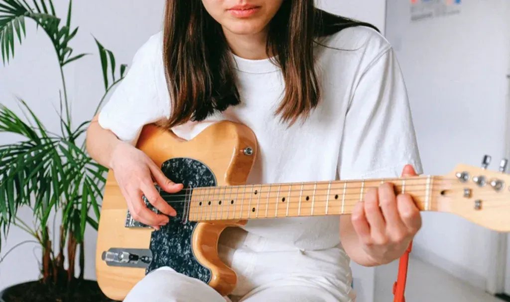 Joven tocando una guitarra eléctrica de cuerpo natural sentada junto a una planta