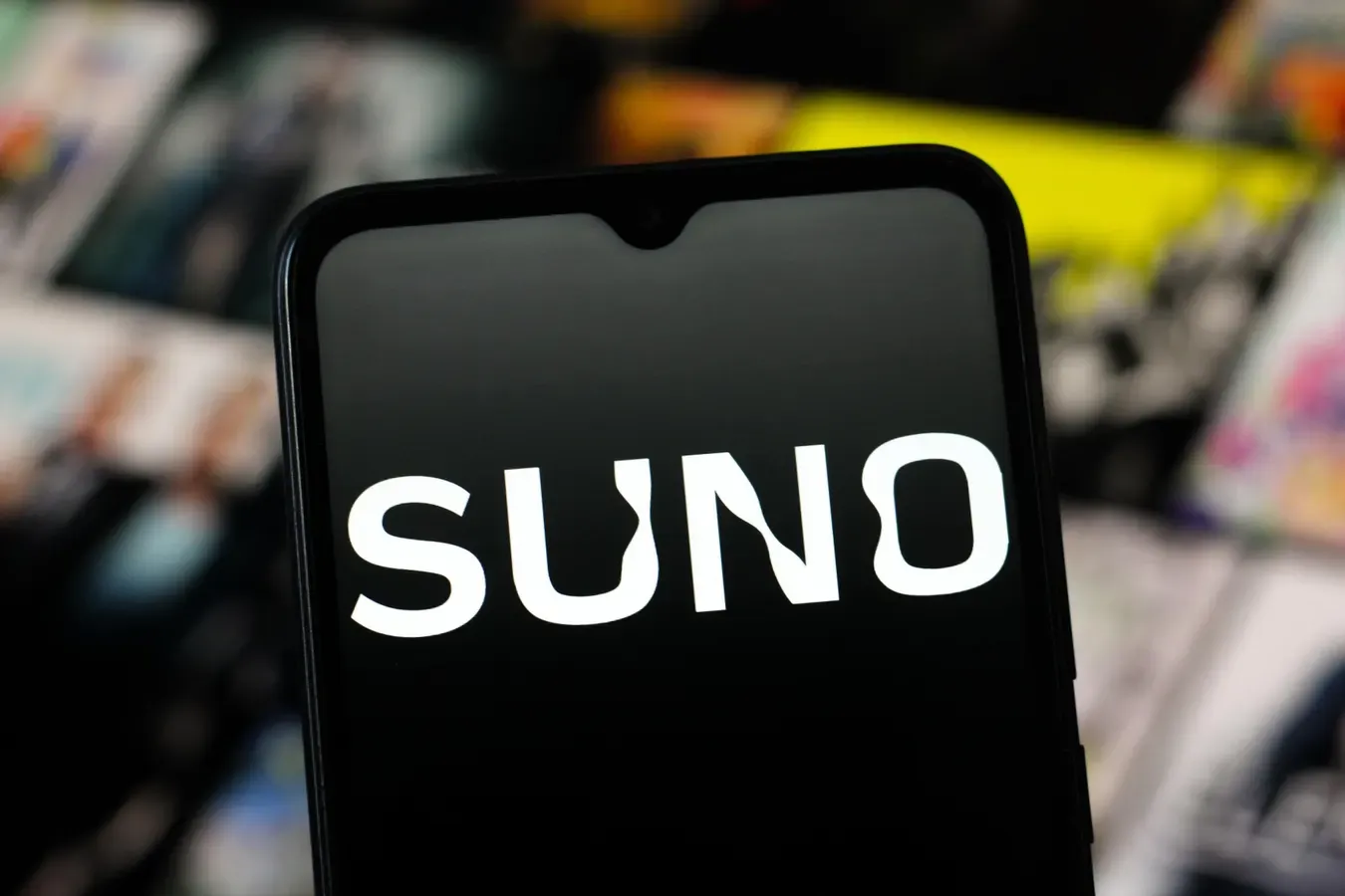 Celular con el logo de Suno en letras blancas sobre fondo negro, con portadas de discos desenfocadas detrás