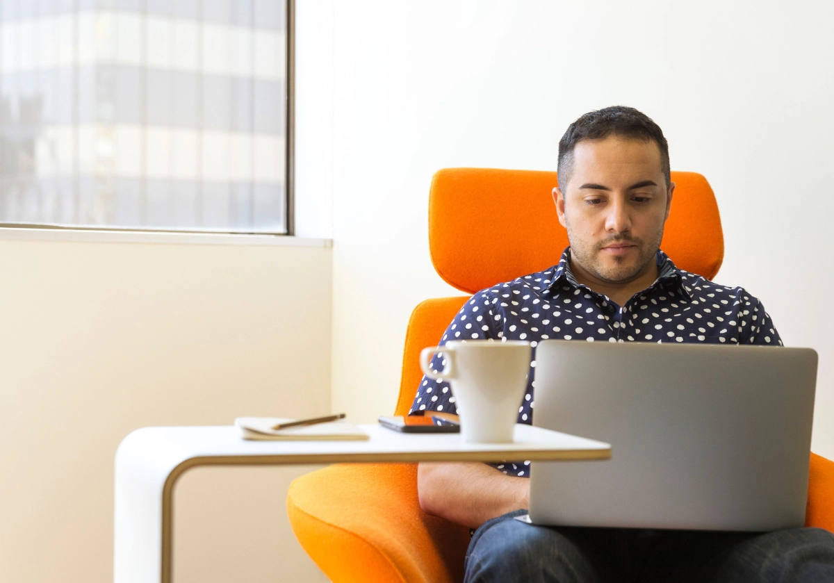 Estudiante trabajando en su laptop en un sillón naranja